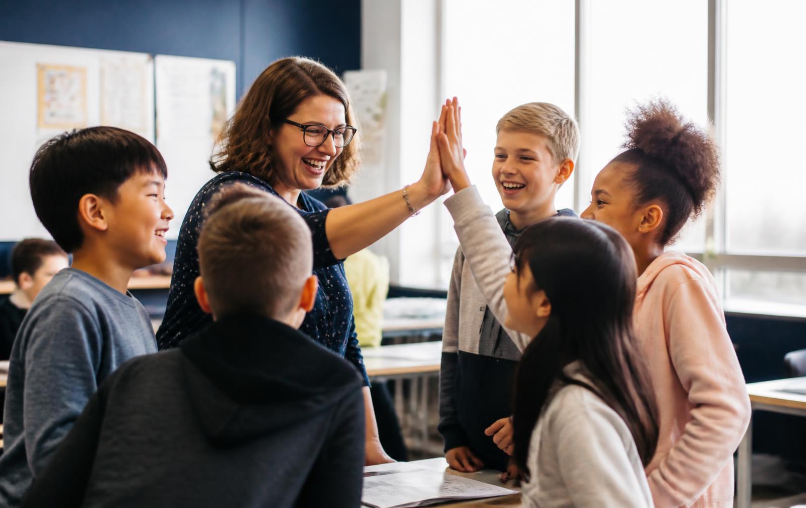 A teacher celebrating with elementary students in a bright classroom